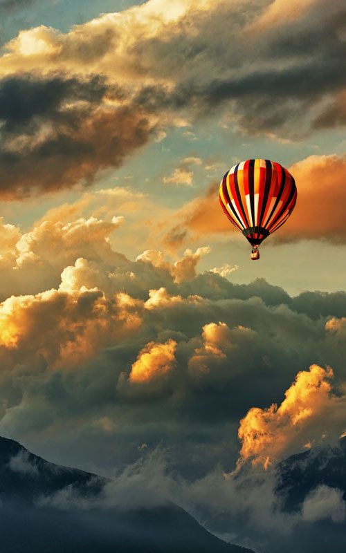 A hot-air balloon in front of several clouds over mountains