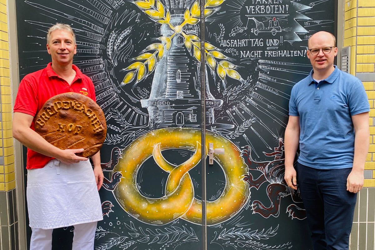 Two men are standing smiling in front of the door of a bakery