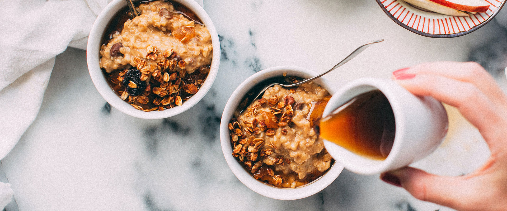 Ahornsirup wird über zwei Schüsseln mit frischem Porridge gegossen